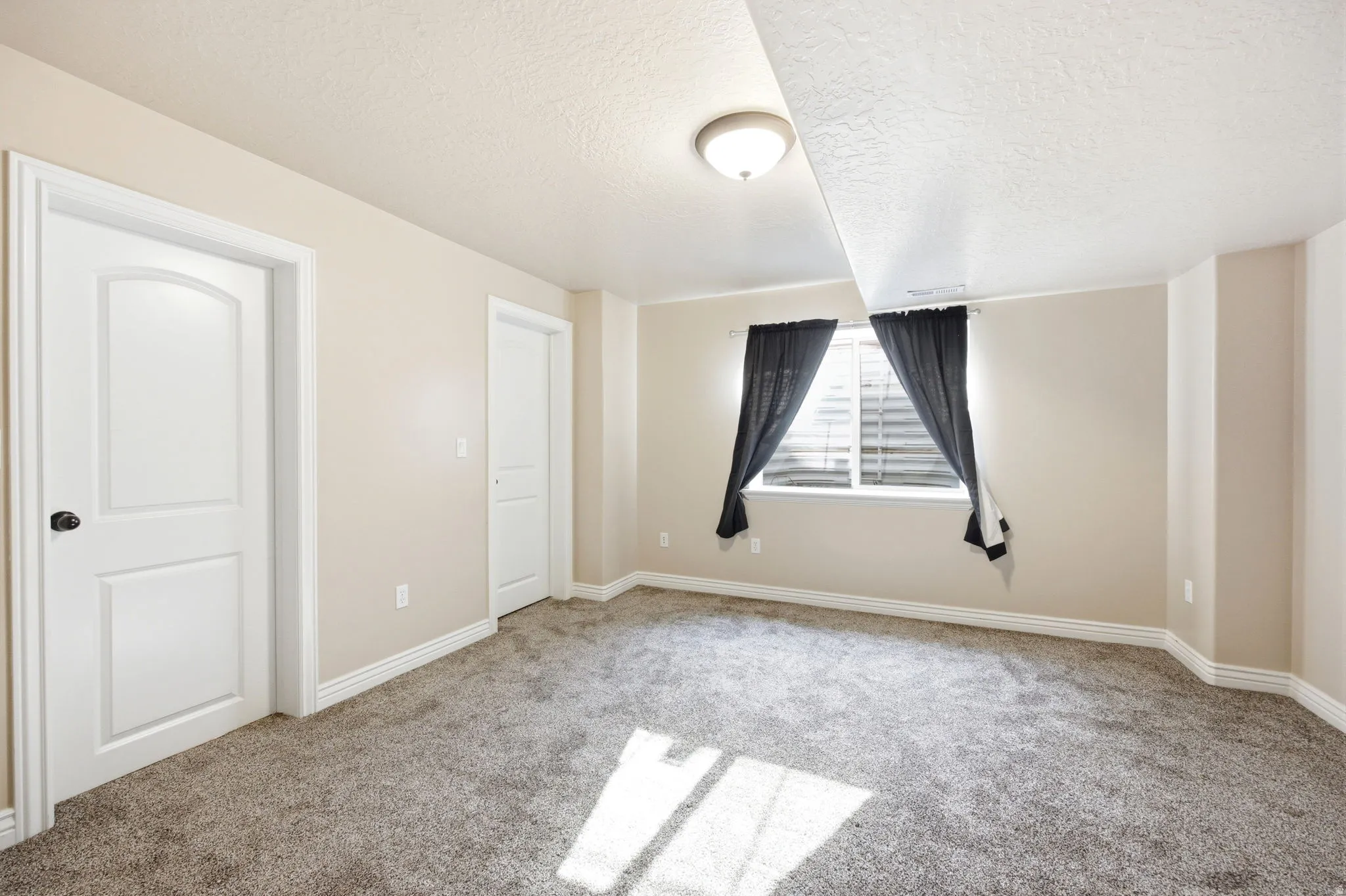 Carpeted room with a window featuring horizontal blinds and dark drapes