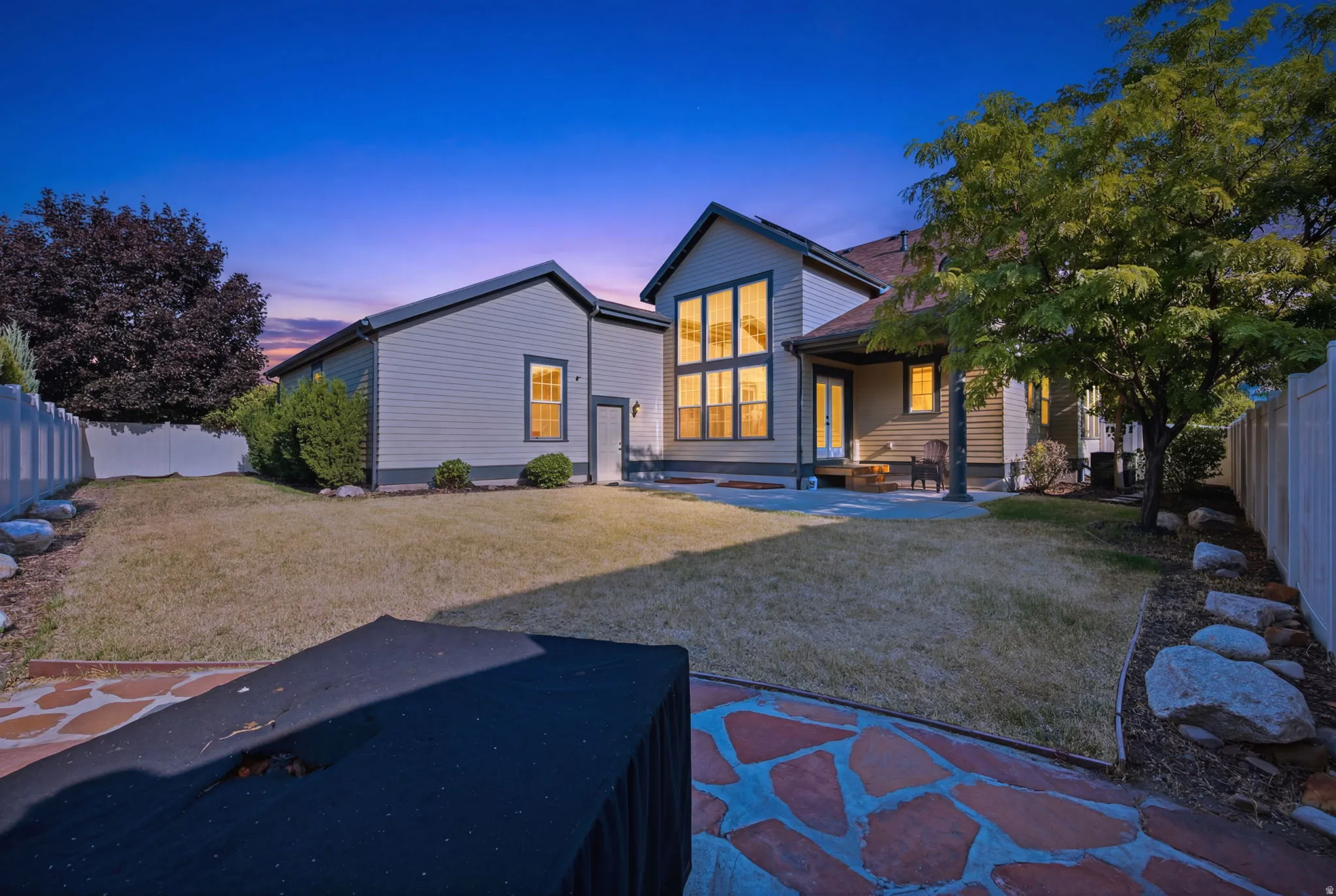 Expansive backyard featuring a manicured lawn, established perimeter landscaping, and a flagstone patio