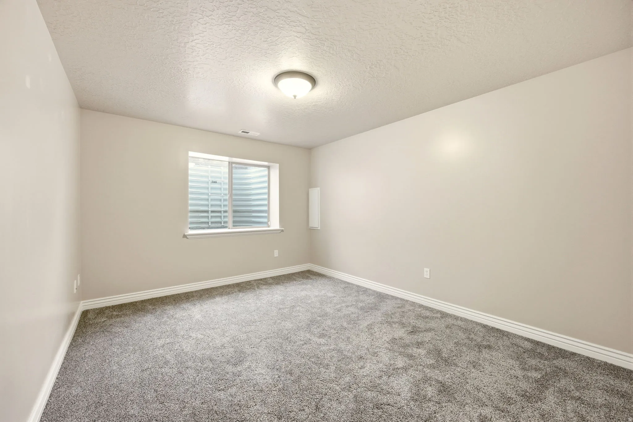 Neutral-toned room featuring a single window with blinds, light gray carpet, and white baseboards