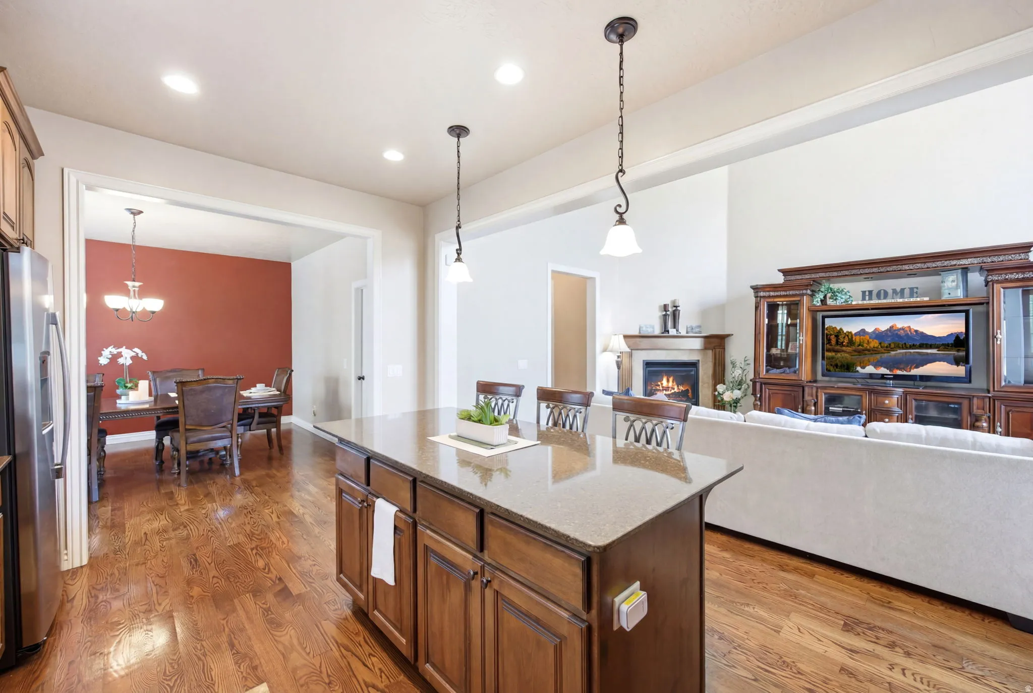 Open-concept living area featuring a kitchen island with seating, dark wood-finish cabinetry, wood-finish flooring, recessed lighting, and a fireplace with a mantel
