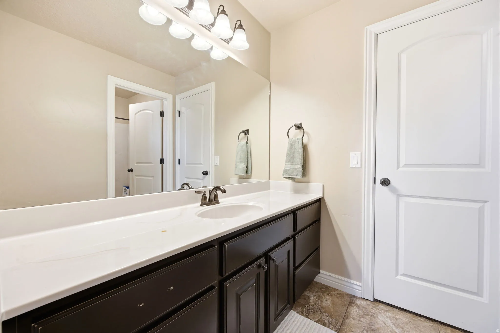 Bathroom vanity featuring a white countertop with integrated sink, dark wood-finish cabinetry, and a bronze-finish faucet
