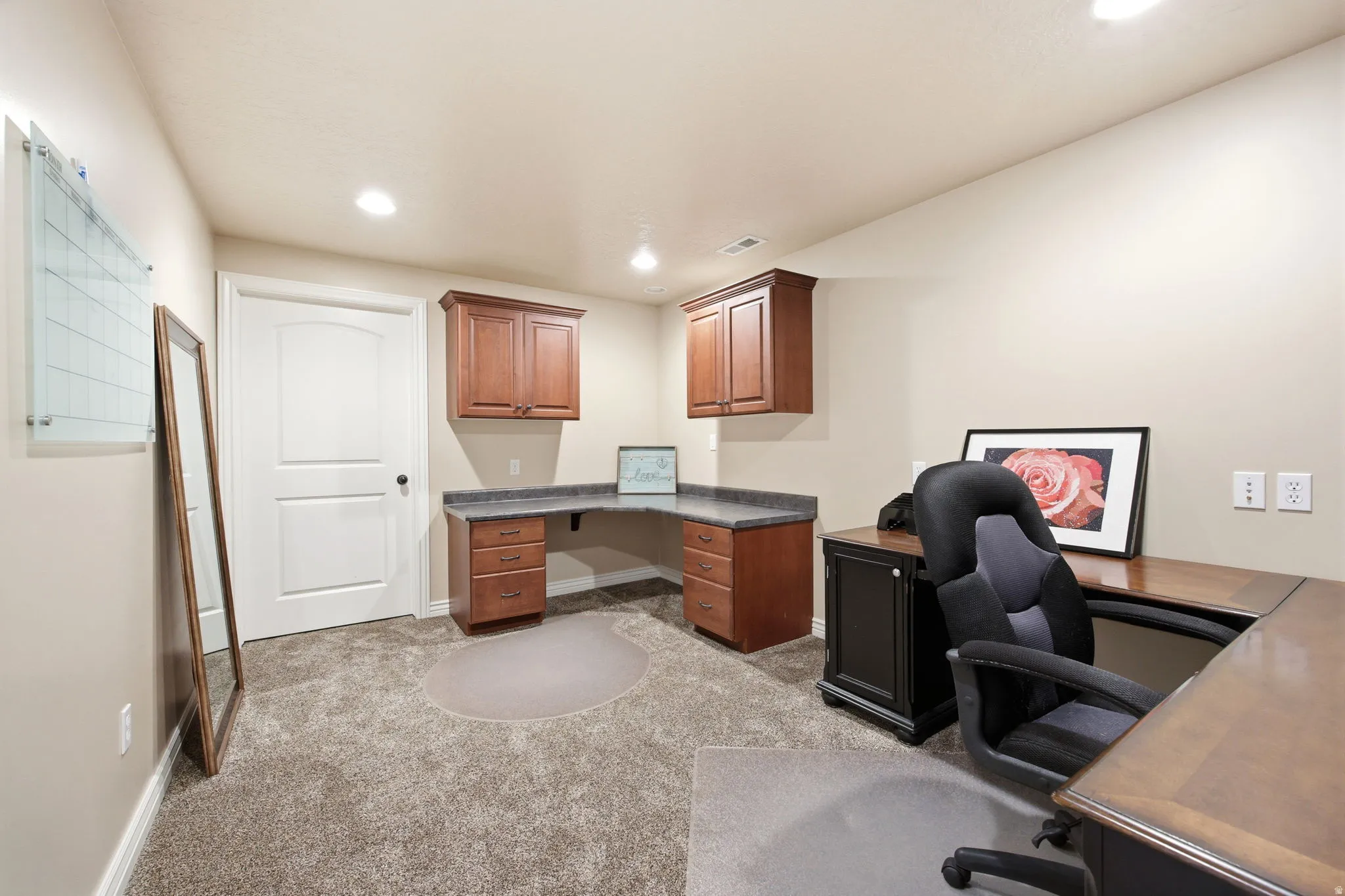 Dedicated office space featuring built-in wood cabinetry, a wrap-around desk with a stone-finish countertop, and plush carpeting