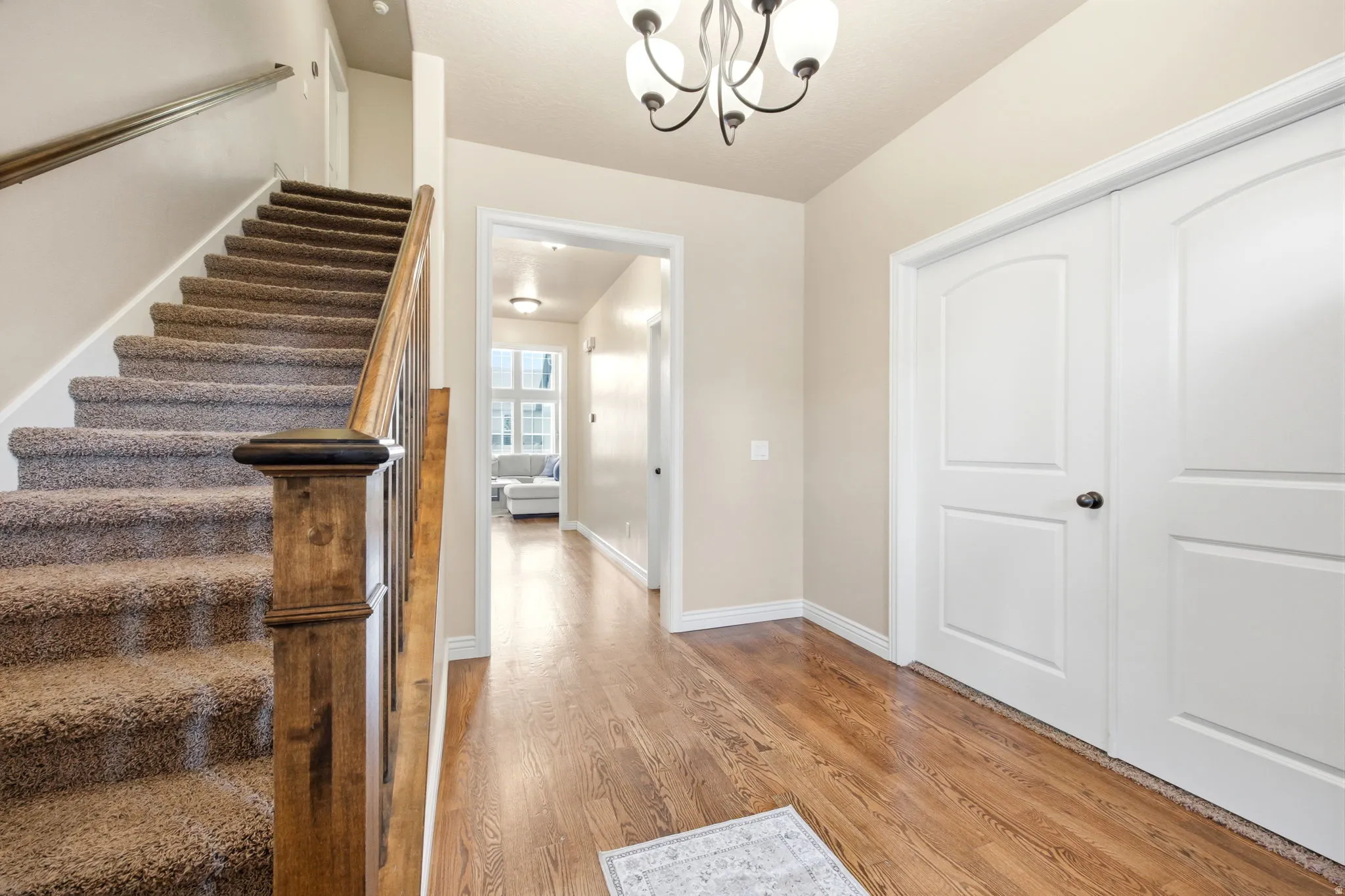 Entryway featuring wood-finish flooring, a carpeted staircase with wood newel post and handrail, and a chandelier with glass shades