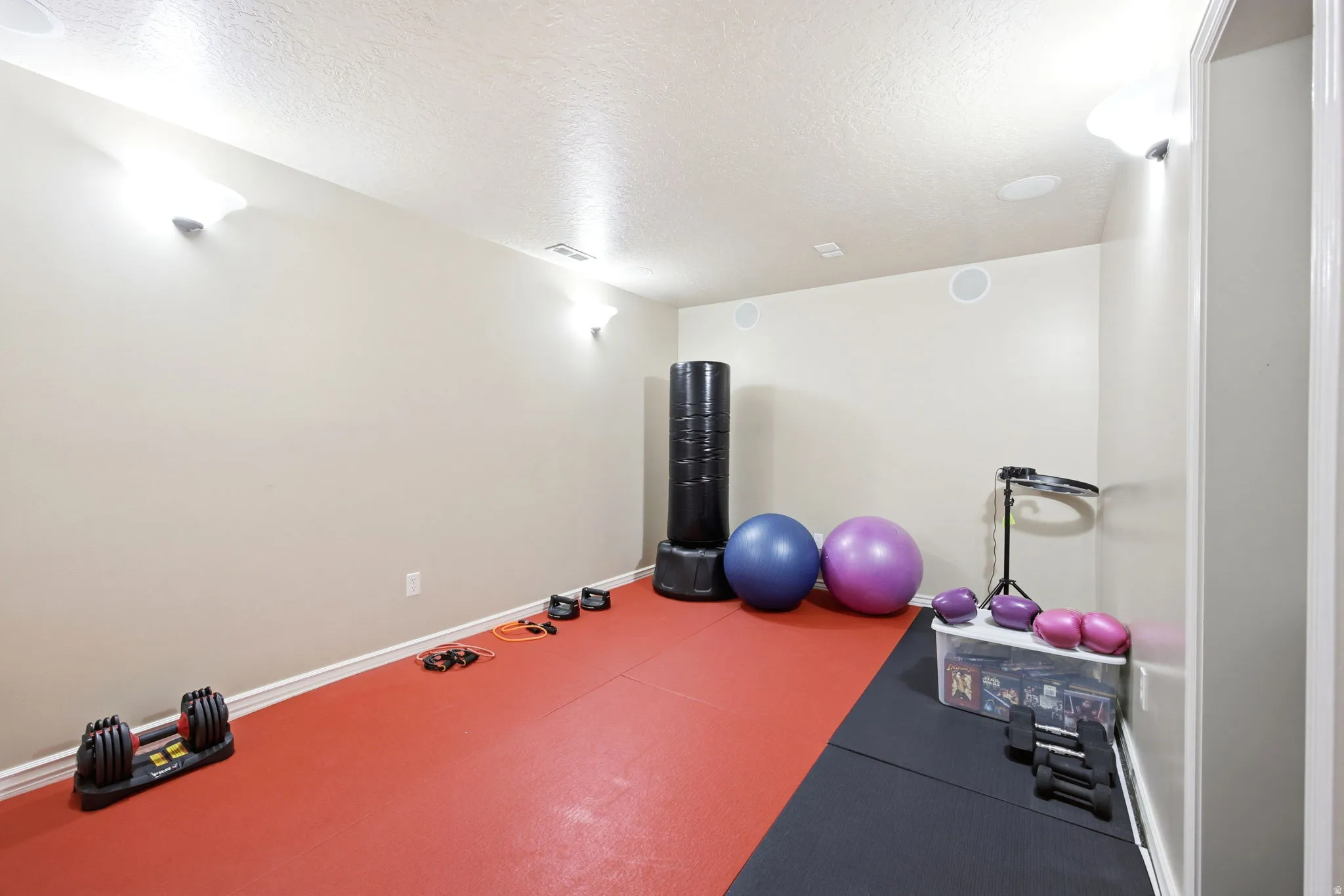 Dedicated exercise space featuring red and black interlocking floor mats, recessed ceiling speakers, and wall-mounted sconce lighting