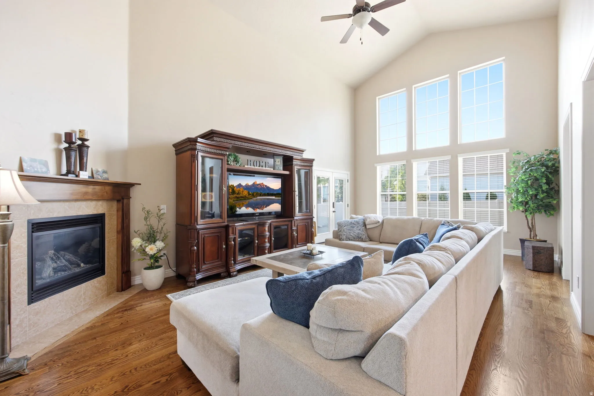 Living area featuring soaring vaulted ceilings, a fireplace with a tile surround and wood mantel, wood-finish flooring, and expansive windows