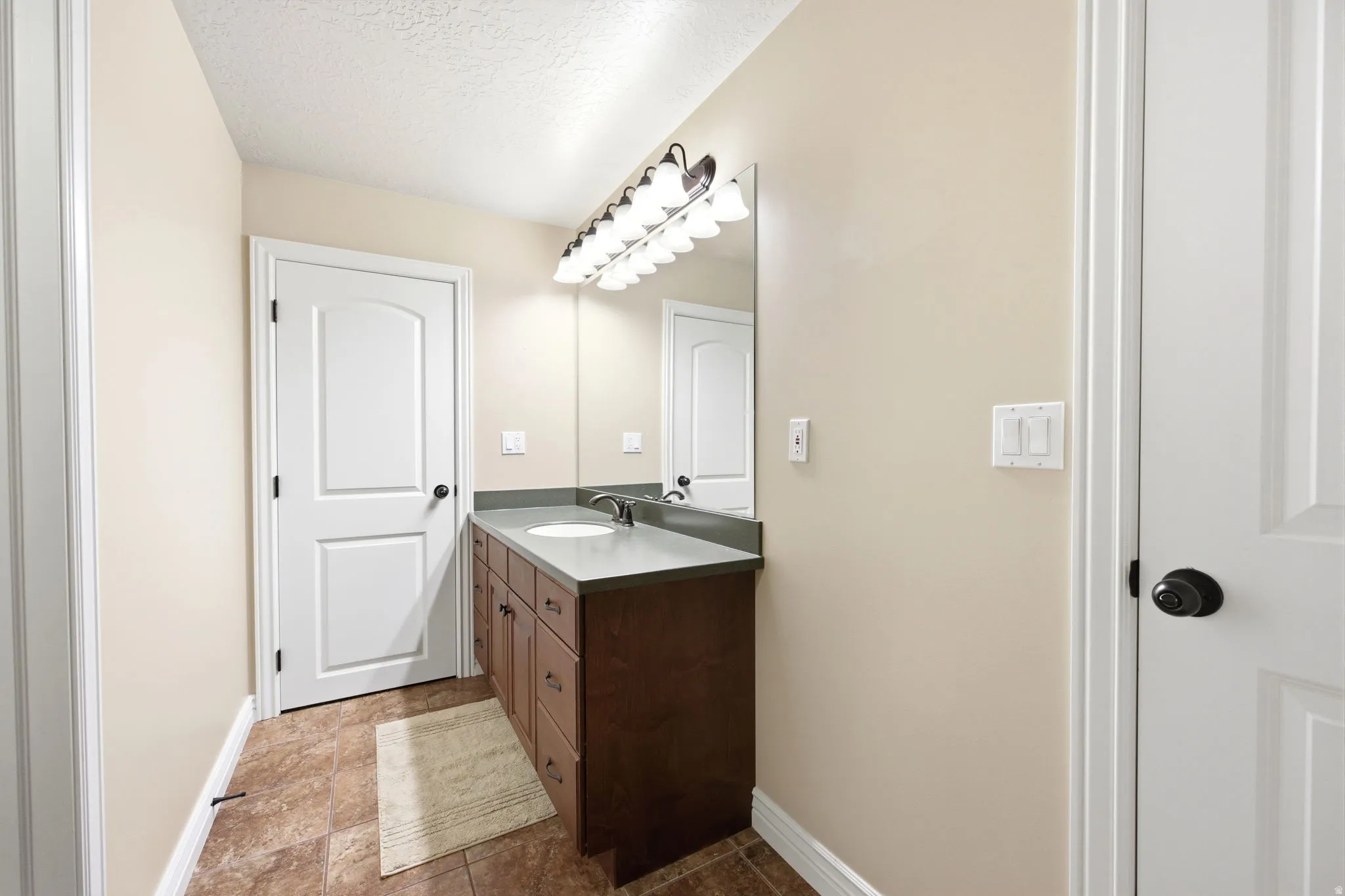 Bathroom featuring a single vanity with wood-finish cabinetry, a grey countertop, and an undermount sink