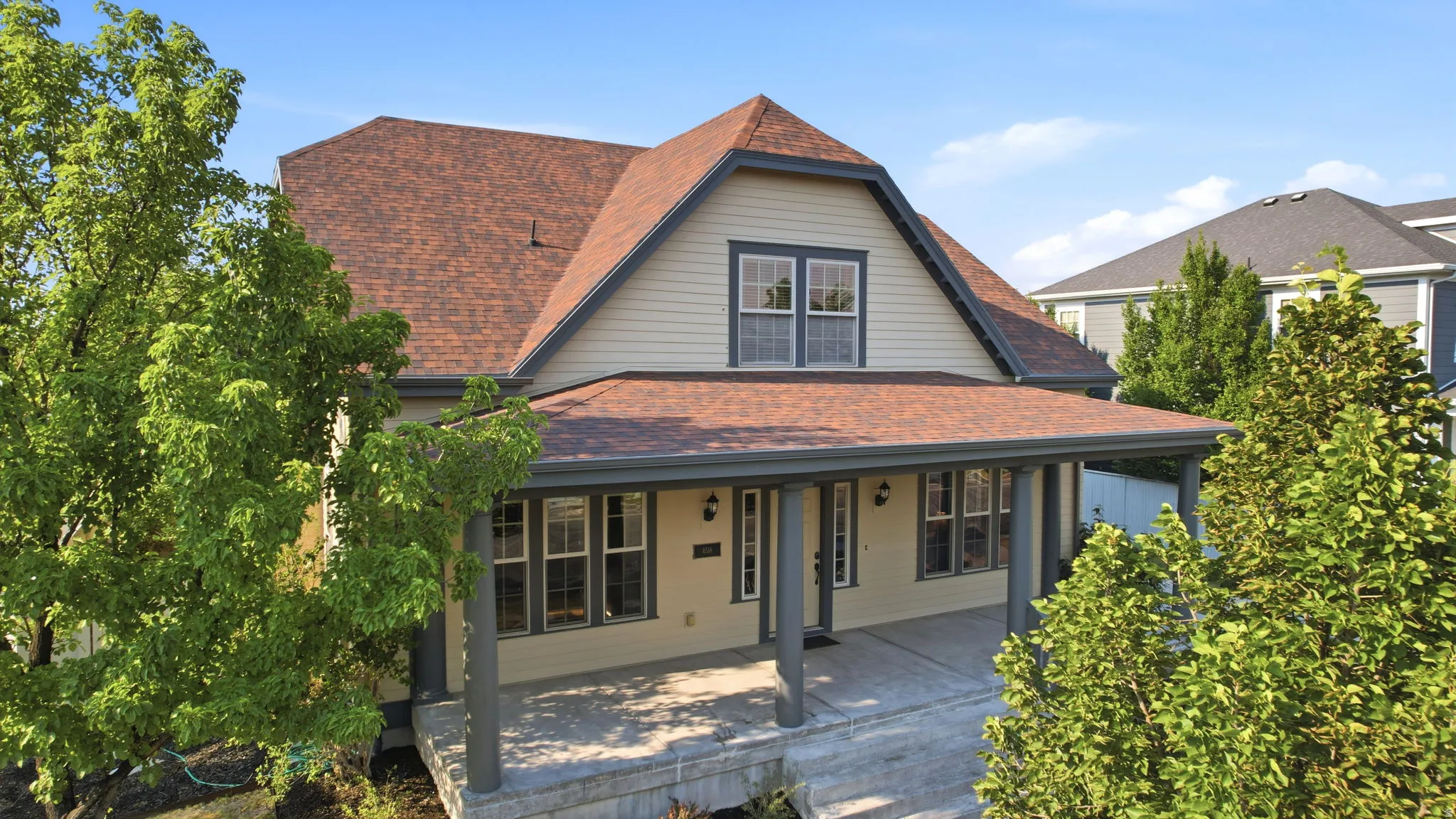 Craftsman-style residence with a prominent covered front porch, light-colored siding, and a contrasting dark brown roof