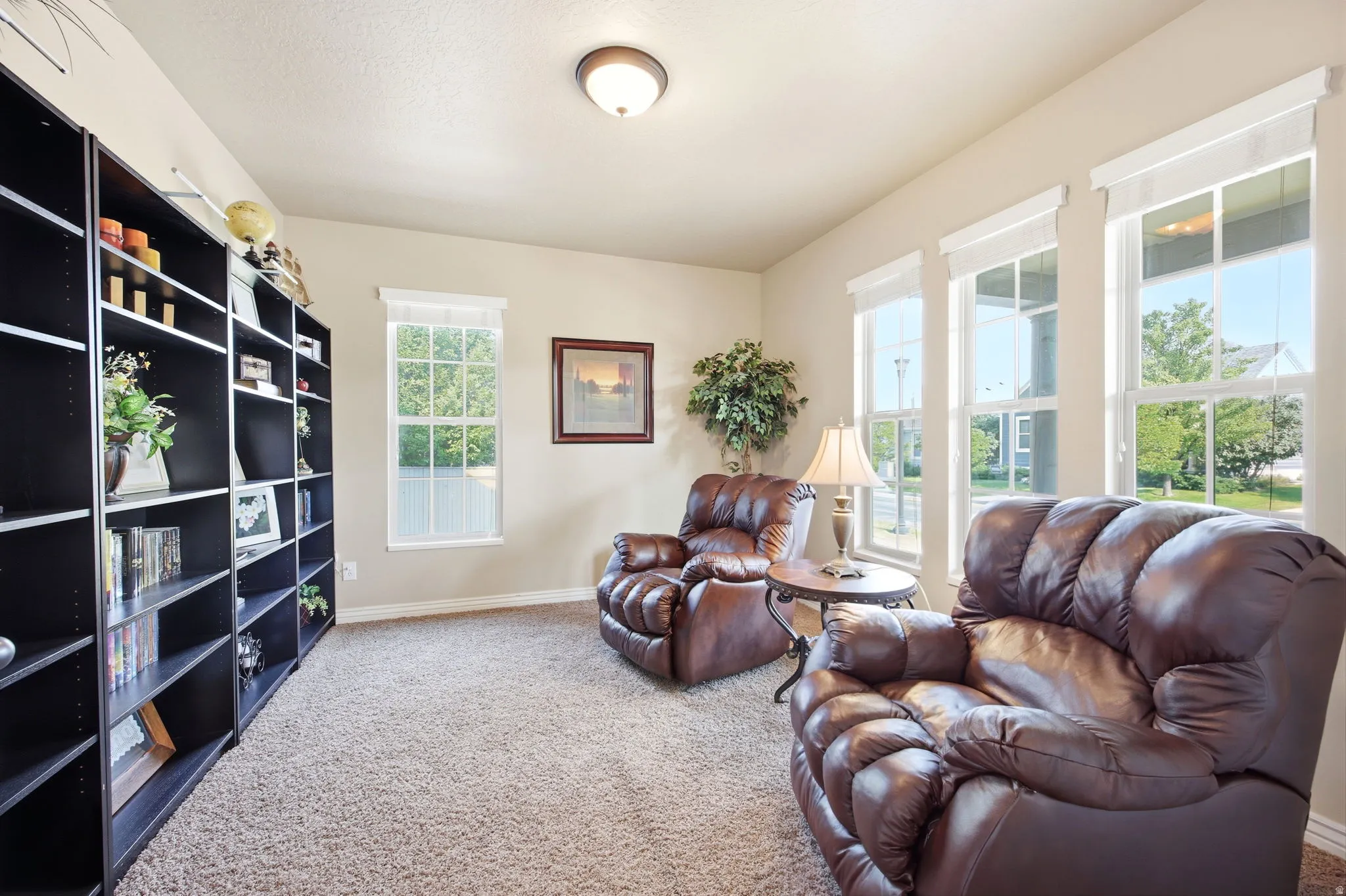 Bright interior room featuring a wall of built-in shelving, four windows providing natural light, and neutral wall paint