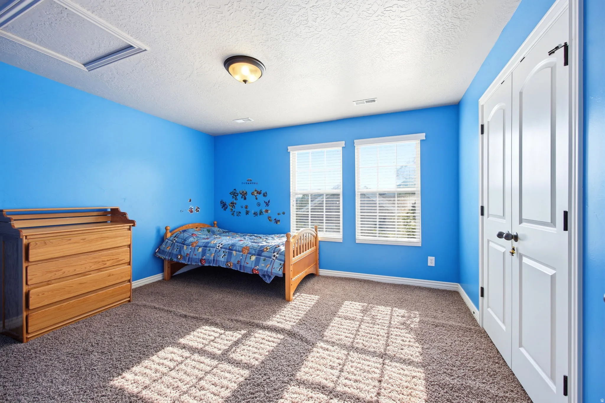 Carpeted room featuring two windows with blinds, a ceiling-mounted light fixture, and a double-door closet with arch paneling