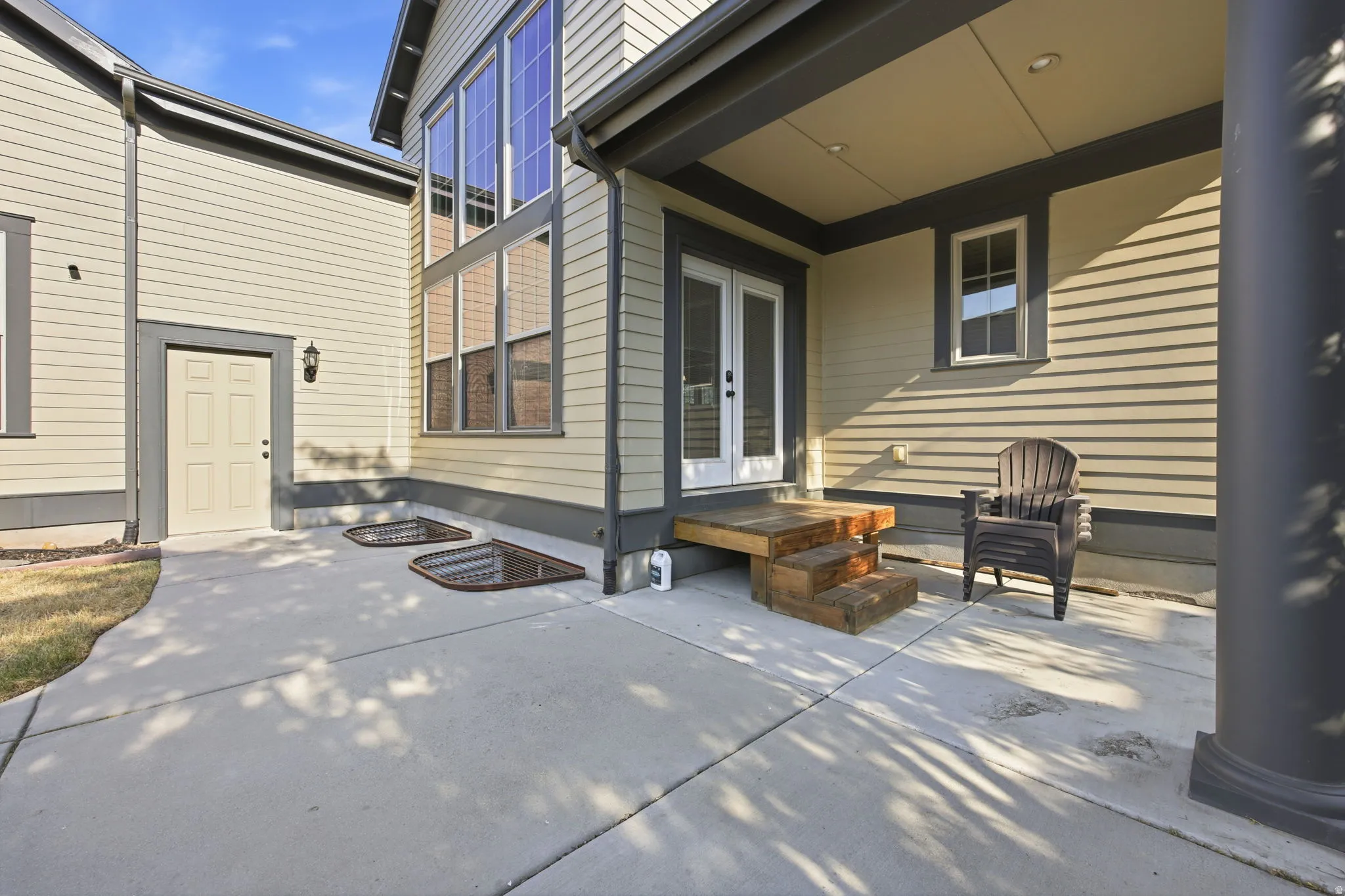 Exterior patio area featuring a two-step wood entry to french doors, light beige siding, charcoal trim, and a covered porch