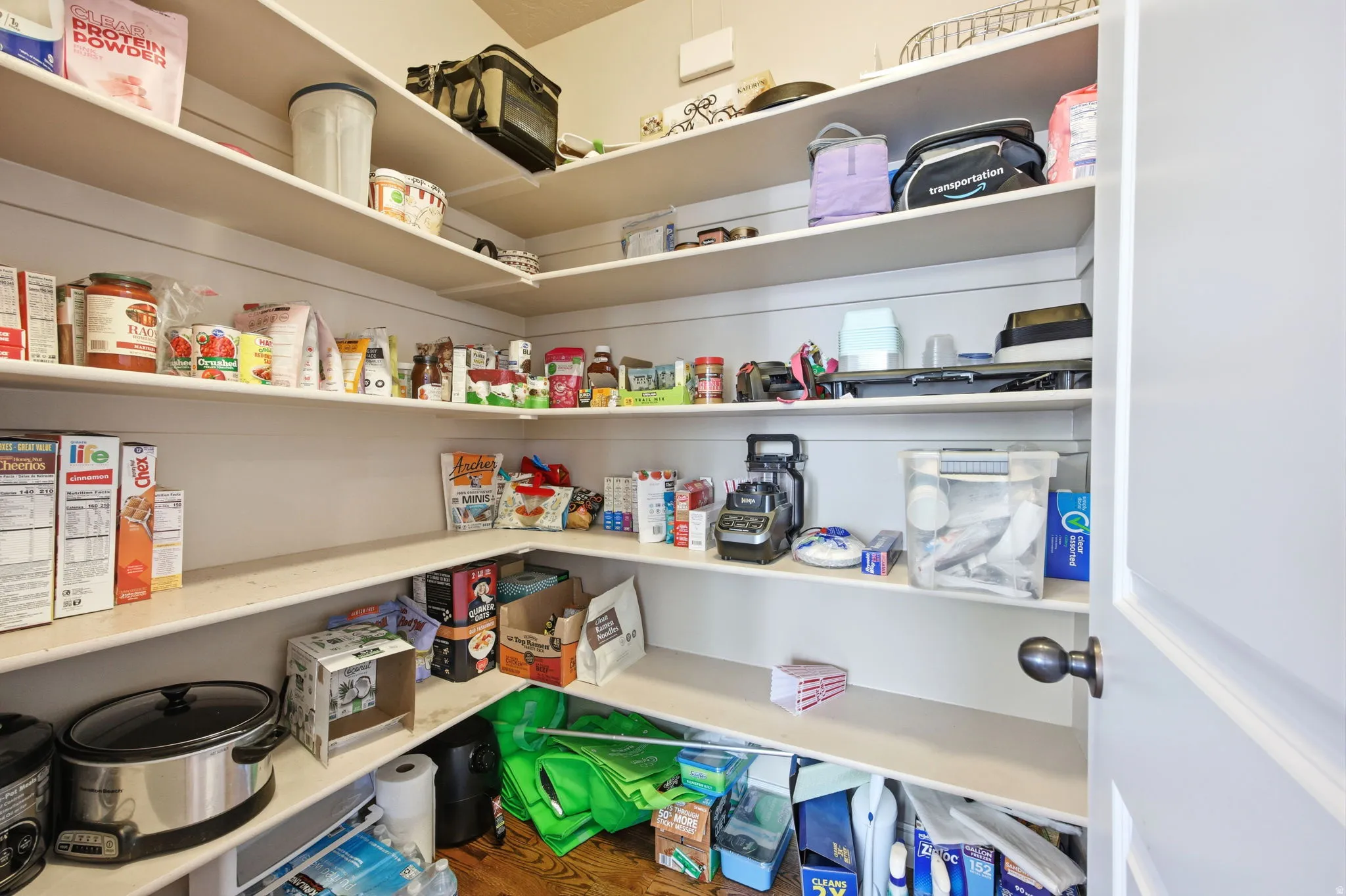 Walk-in pantry featuring extensive built-in shelving, white painted walls, and wood-finish flooring