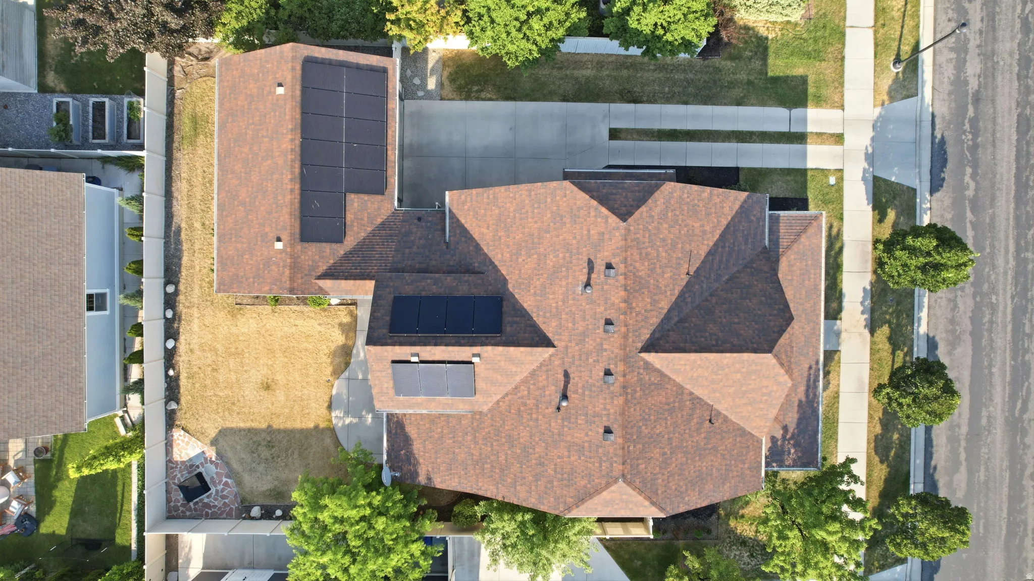 Expansive roofline featuring solar panel arrays, a concrete driveway, and a paved street