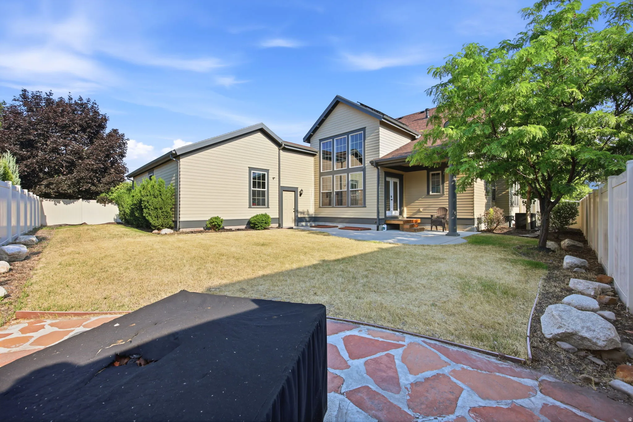 Spacious backyard featuring a stone patio, mature trees, and a privacy fence