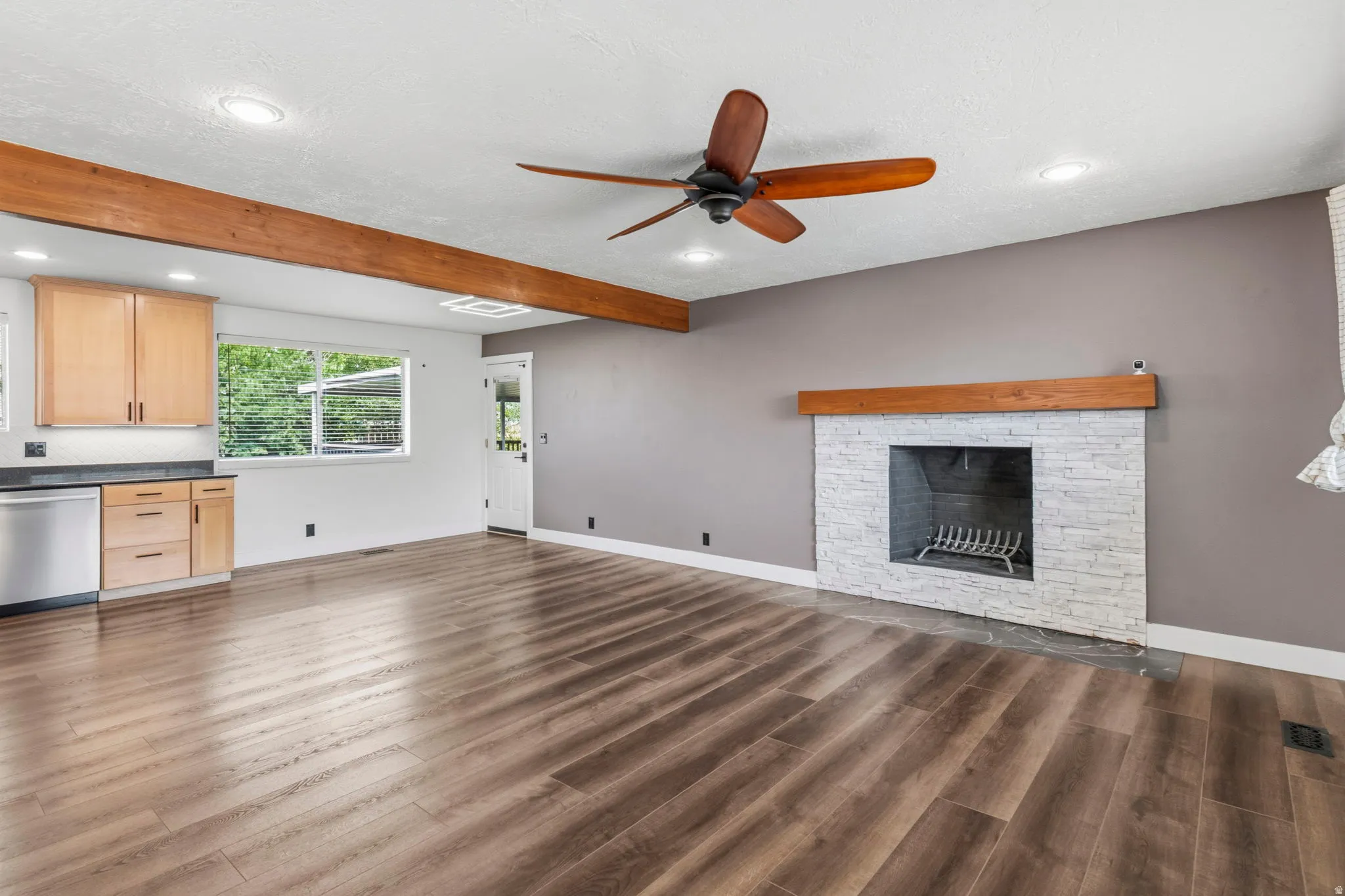 Spacious interior featuring wood-finish flooring, a white brick fireplace with a wood mantel, a ceiling fan, and recessed lighting