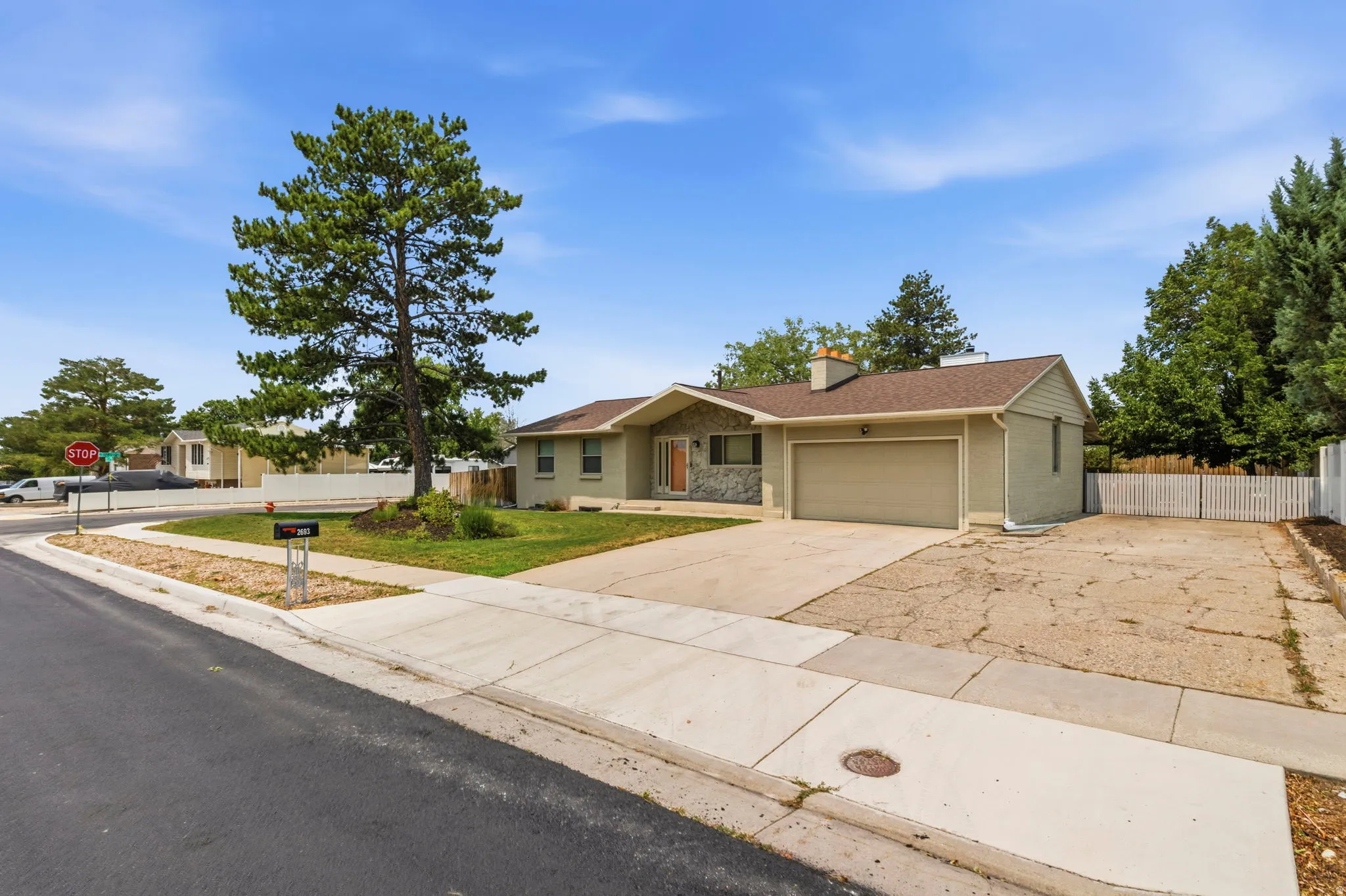 Ranch-style exterior featuring a stone facade accent, an attached garage, a paved driveway, and mature landscaping