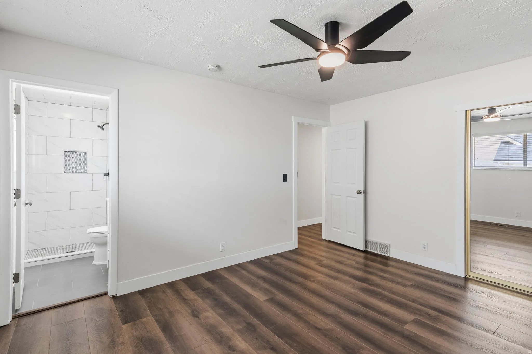 Spacious room featuring wood-finish flooring, a modern black ceiling fan with integrated lighting, and a mirrored closet door
