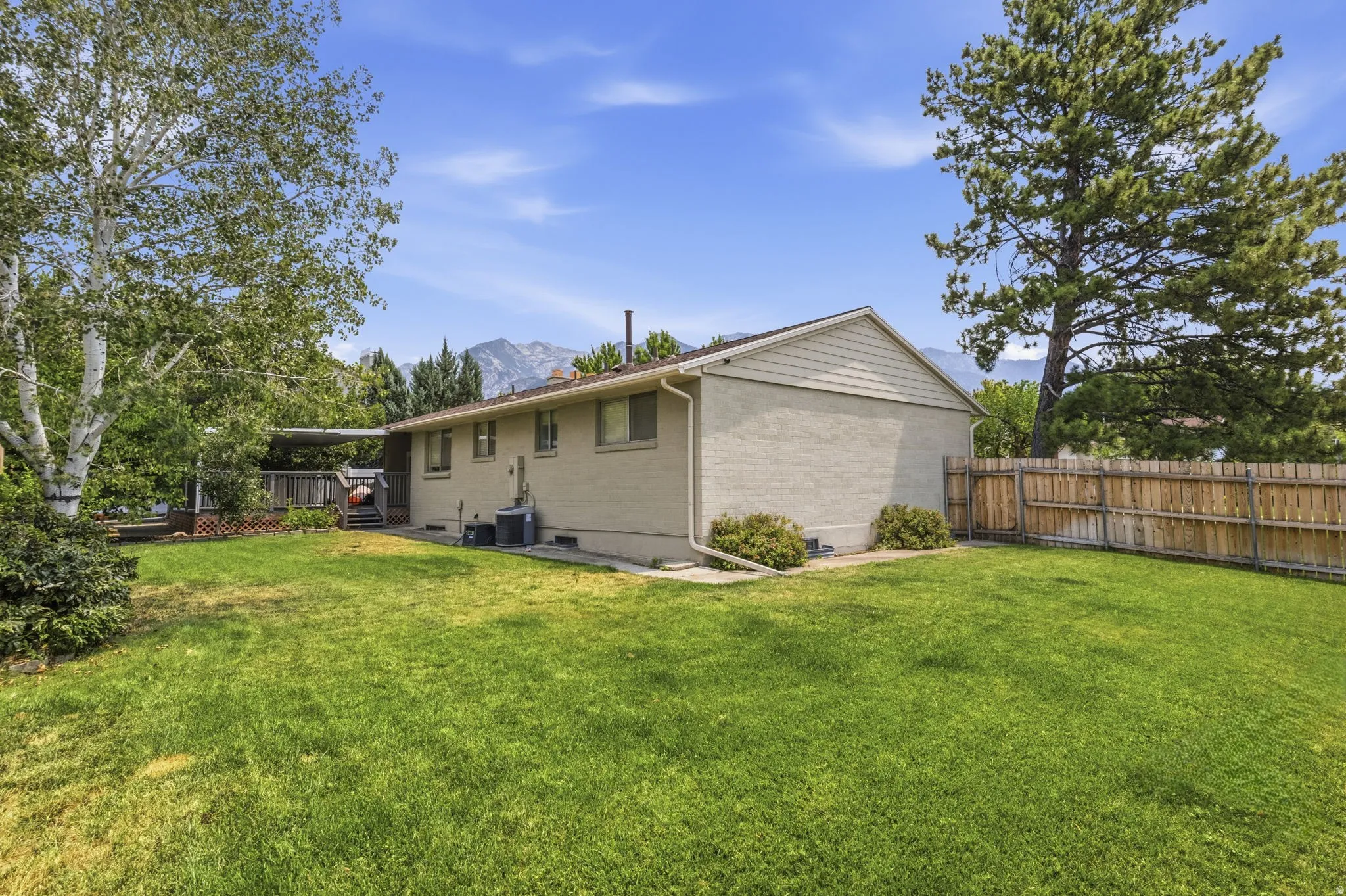 Expansive backyard featuring a green lawn, mature trees, and a wood privacy fence