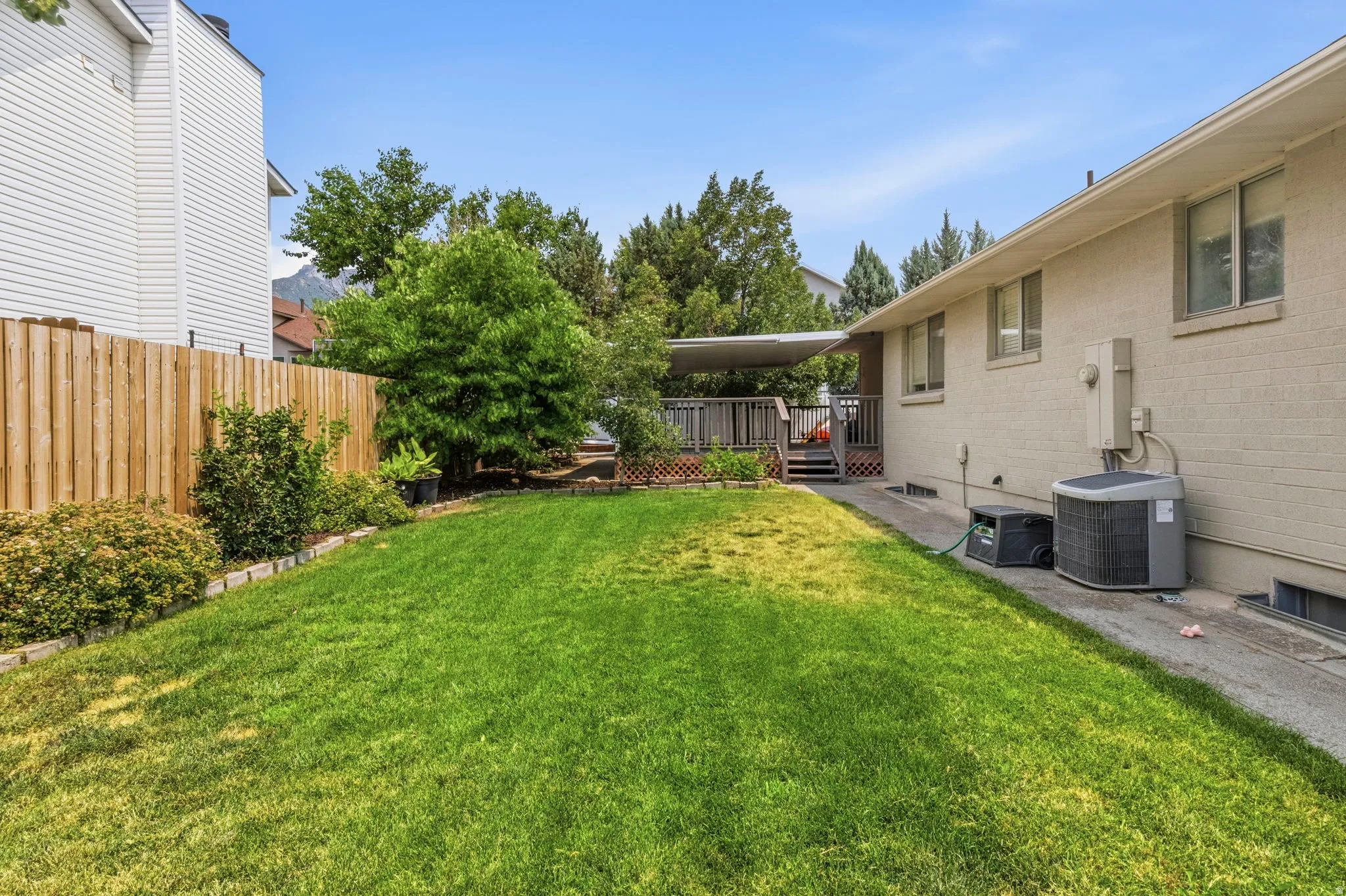 Expansive grassy yard area featuring a wooden privacy fence, established shrubbery, and mature trees