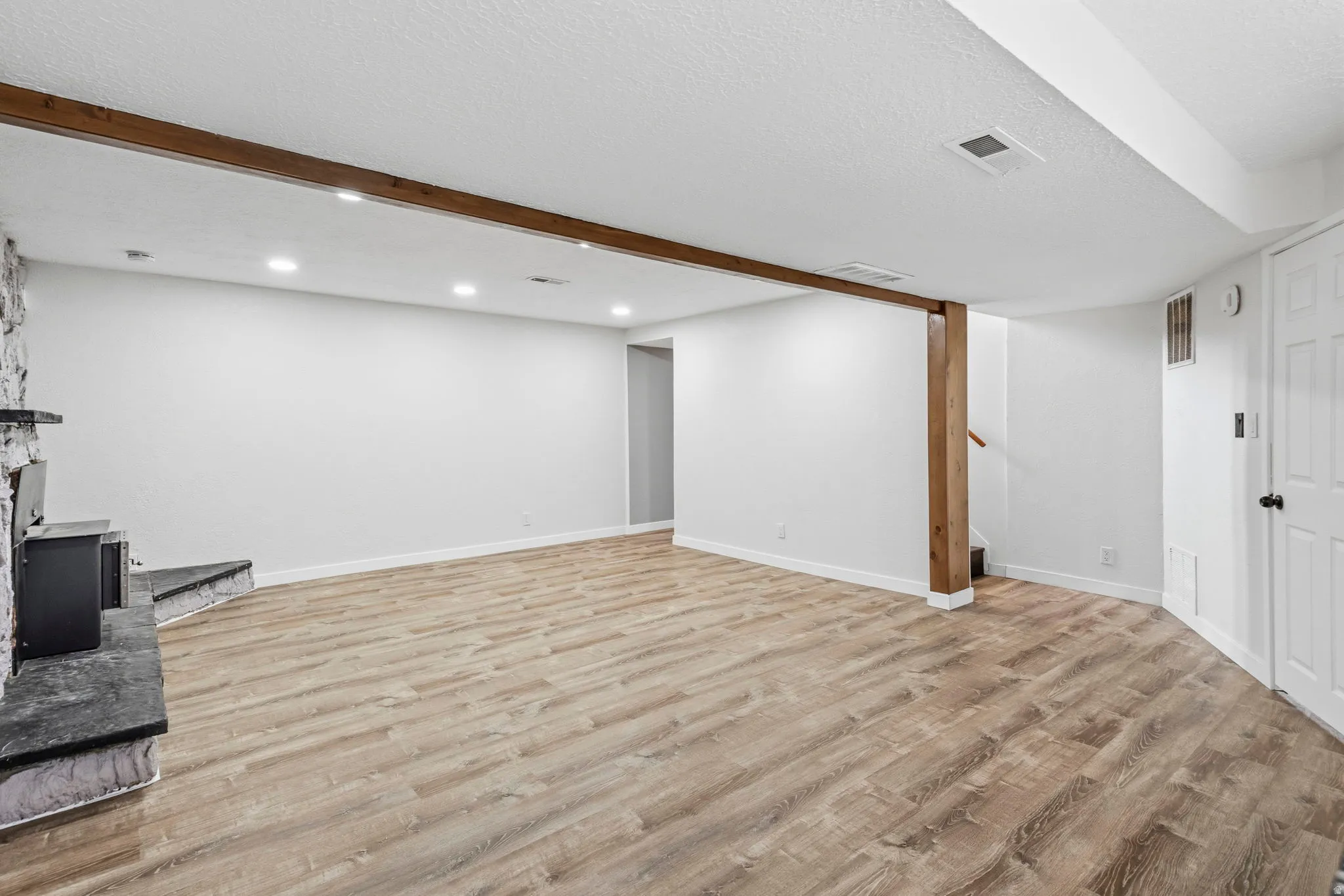 Spacious room featuring wood-finish flooring, recessed lighting, and a stone-clad fireplace with a dark mantel