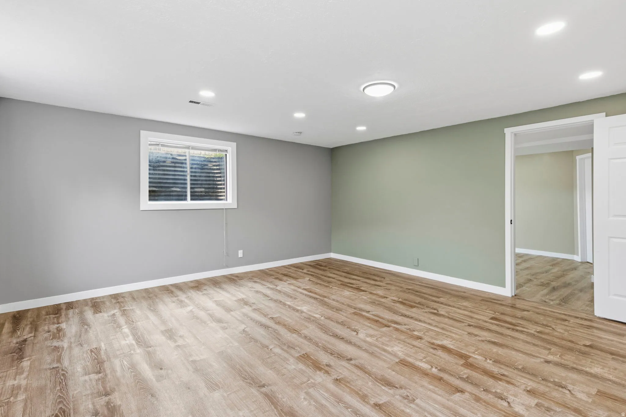 Spacious interior room featuring wood-finish flooring, recessed lighting, and a window with blinds