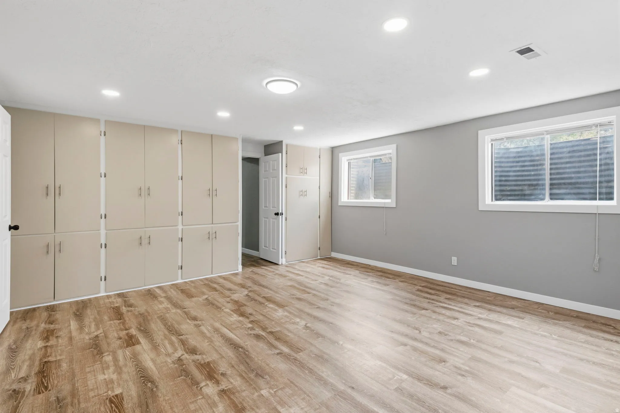 Expansive room featuring extensive built-in cabinetry, wood-finish flooring, two windows, and recessed lighting