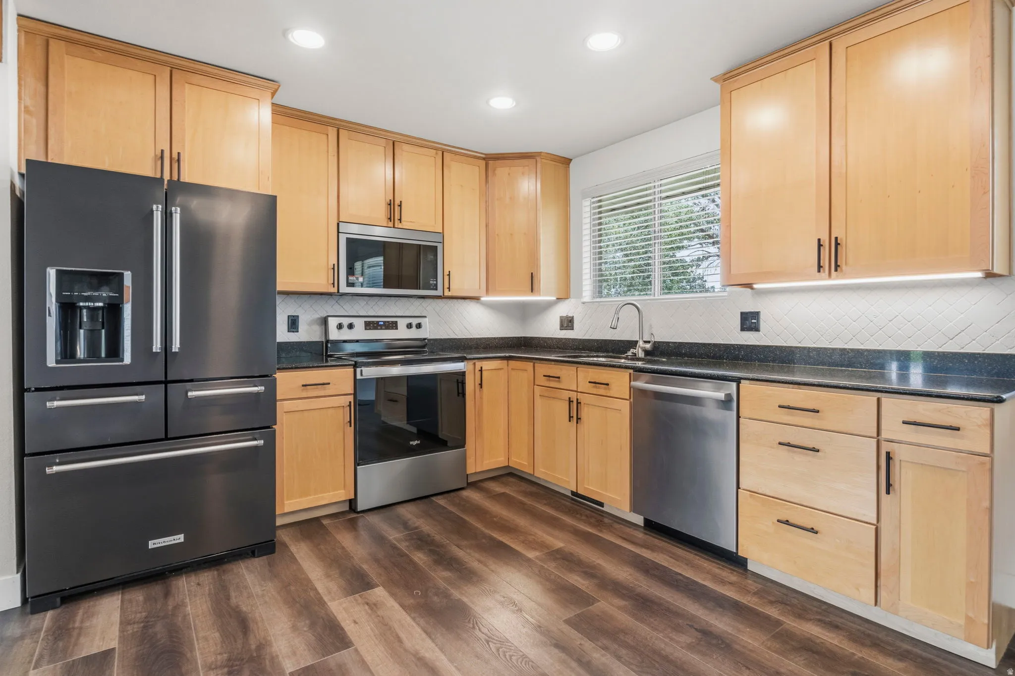 Kitchen featuring wood cabinetry, dark countertops, stainless steel appliances, and wood-finish flooring