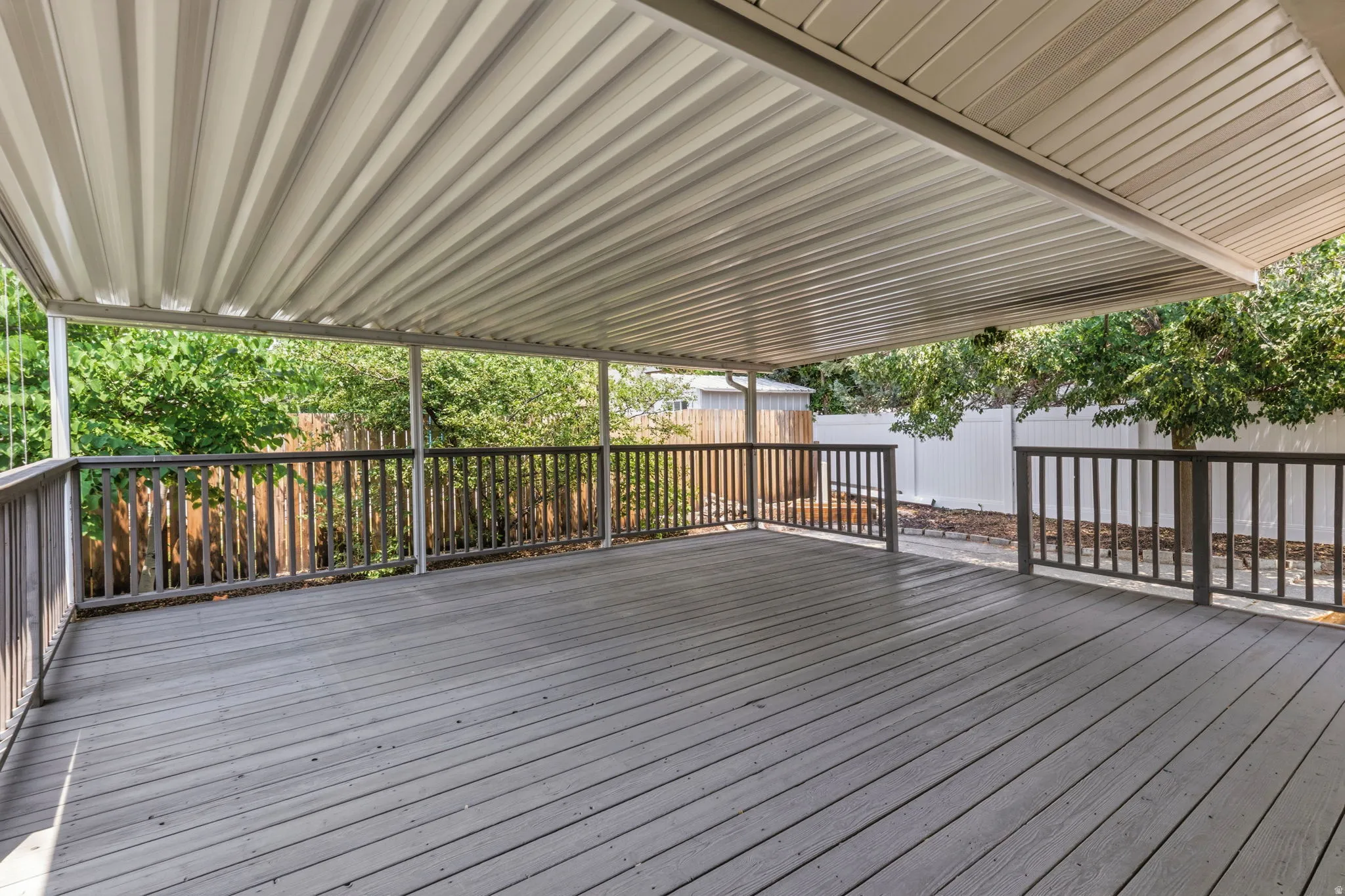 Expansive covered deck featuring gray wood-finish flooring, a white corrugated metal overhead, and dark wood railings