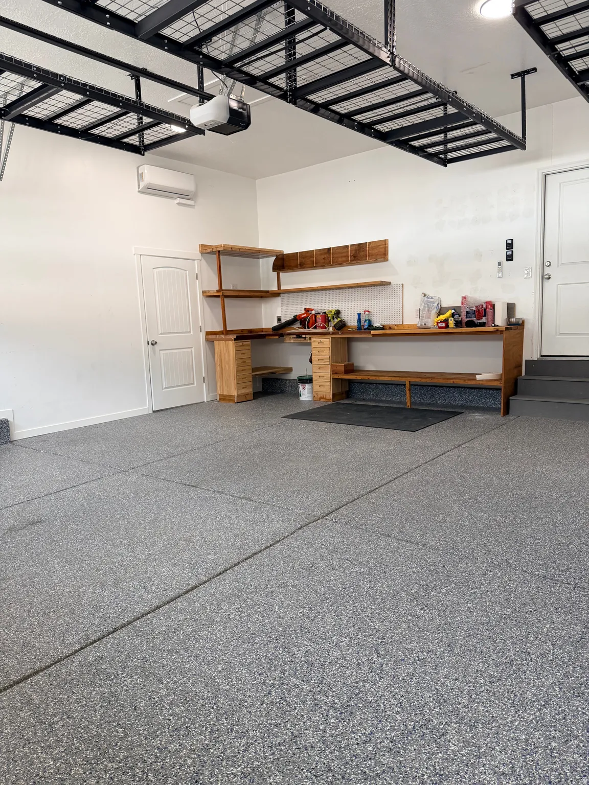 Spacious garage featuring a durable epoxy floor finish, integrated workbench with shelving, mini-split air conditioning unit, and overhead storage racks