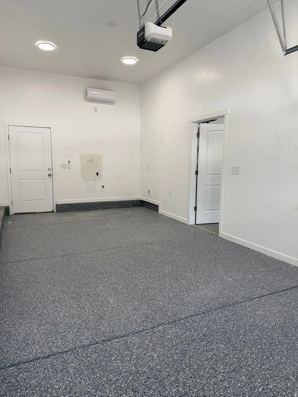 Garage featuring a durable epoxy floor finish, recessed ceiling lighting, a mini-split air conditioning unit, and two interior access doors