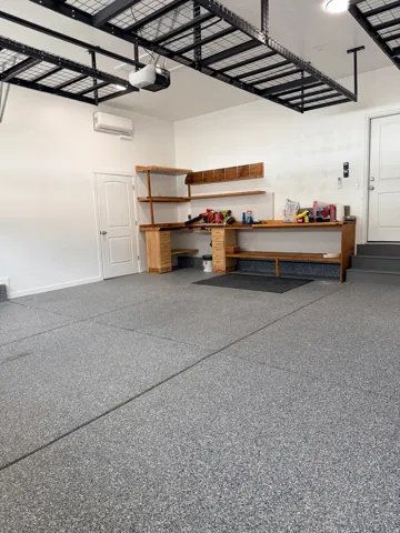 Spacious garage featuring a durable epoxy floor finish, integrated workbench with shelving, mini-split air conditioning unit, and overhead storage racks