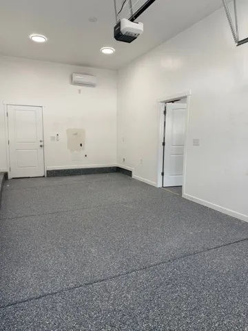 Garage featuring a durable epoxy floor finish, recessed ceiling lighting, a mini-split air conditioning unit, and two interior access doors