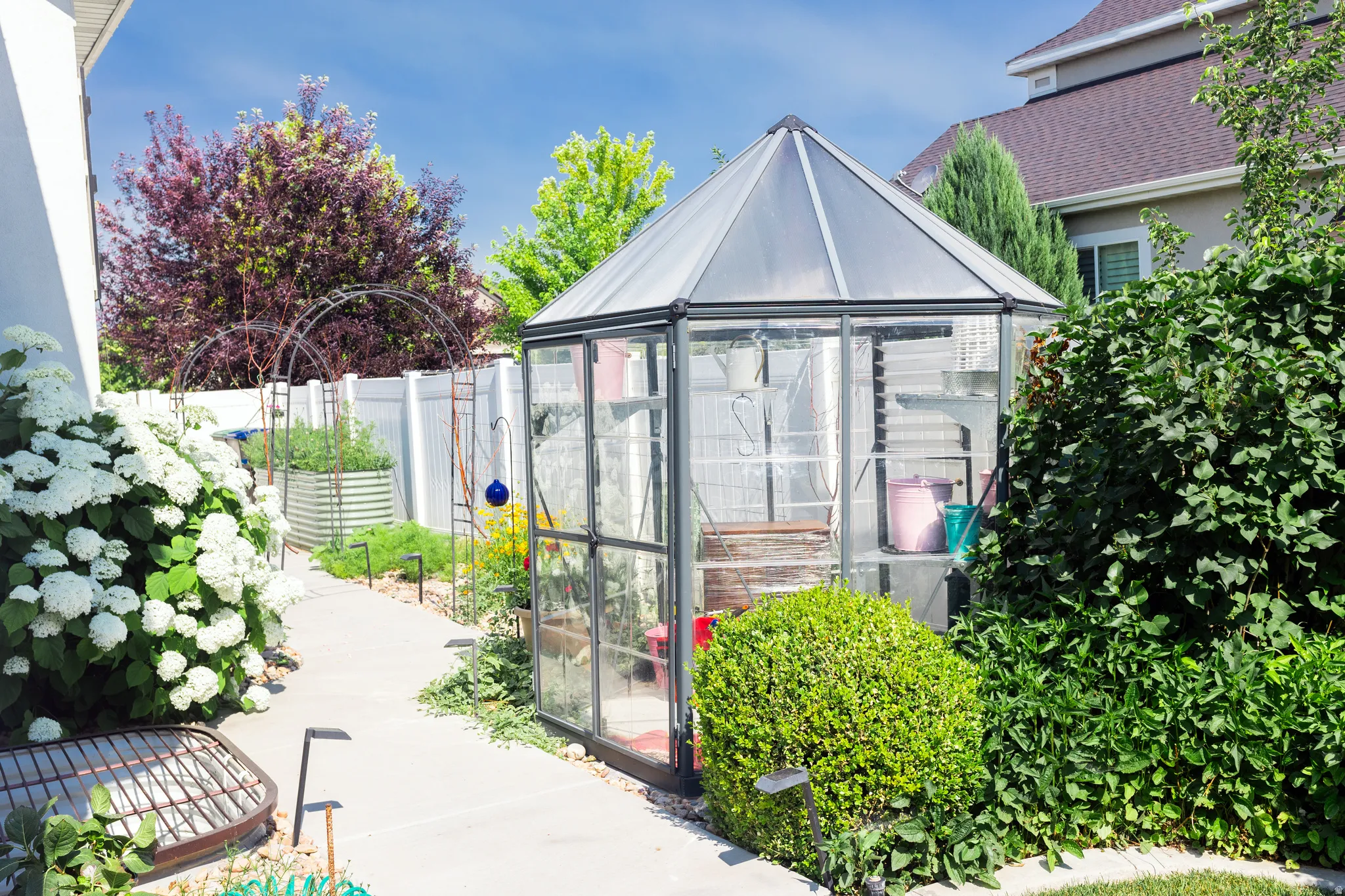 North side of home. Garden path featuring a greenhouse, mature landscaping, white privacy fencing, and raised garden beds