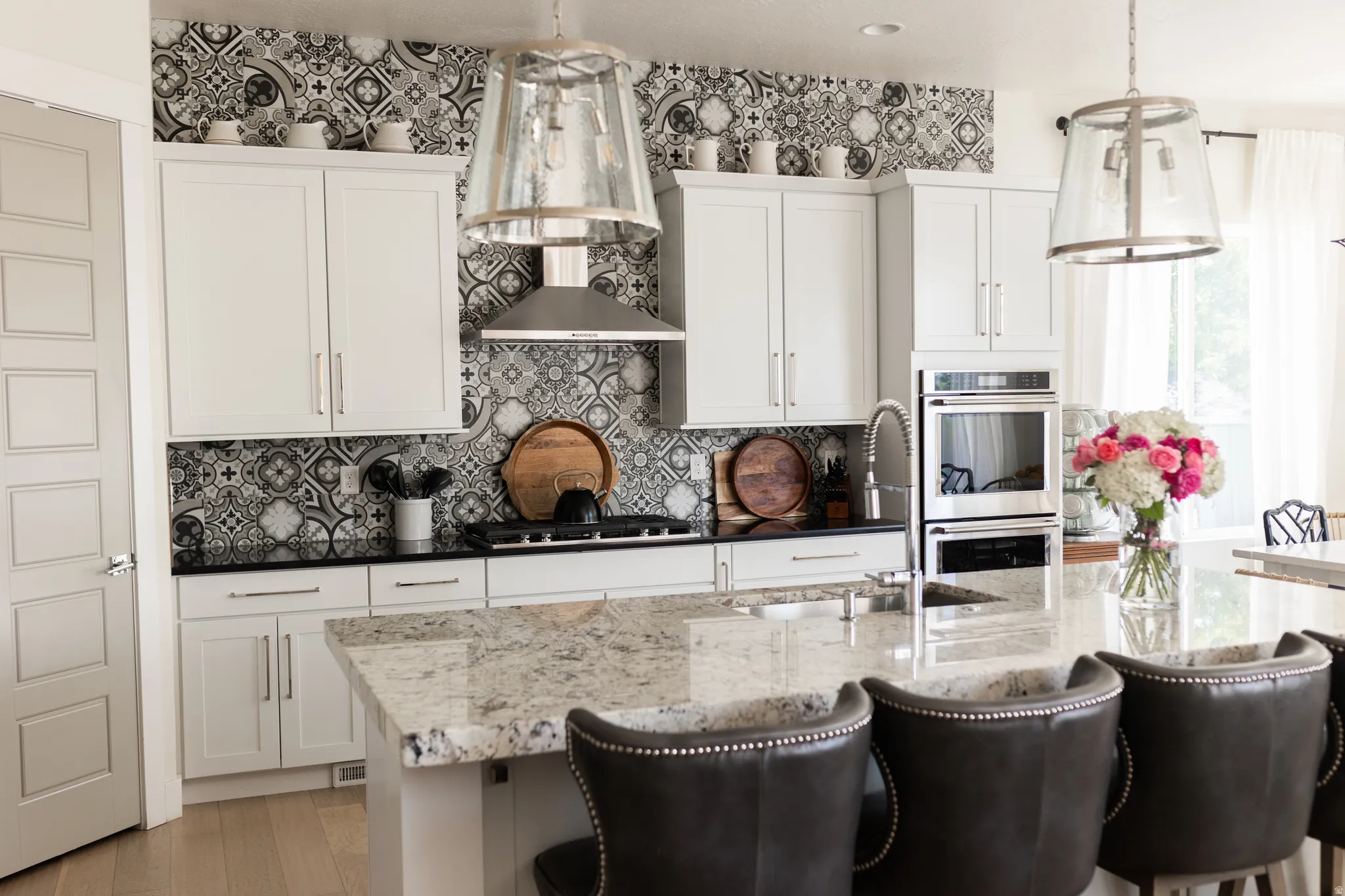 Kitchen featuring a patterned tile backsplash, stainless steel appliances, white cabinetry, a large kitchen island with a stone countertop, and pendant lighting fixtures