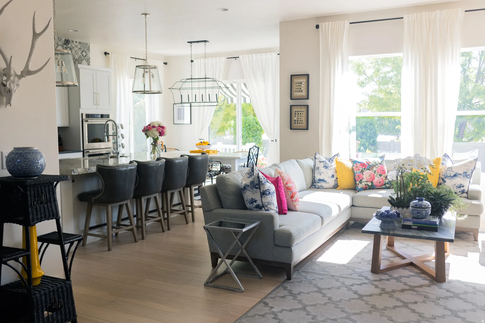 Open-concept living area featuring light wood-finish flooring, a kitchen island with seating, a built-in oven, and white cabinetry