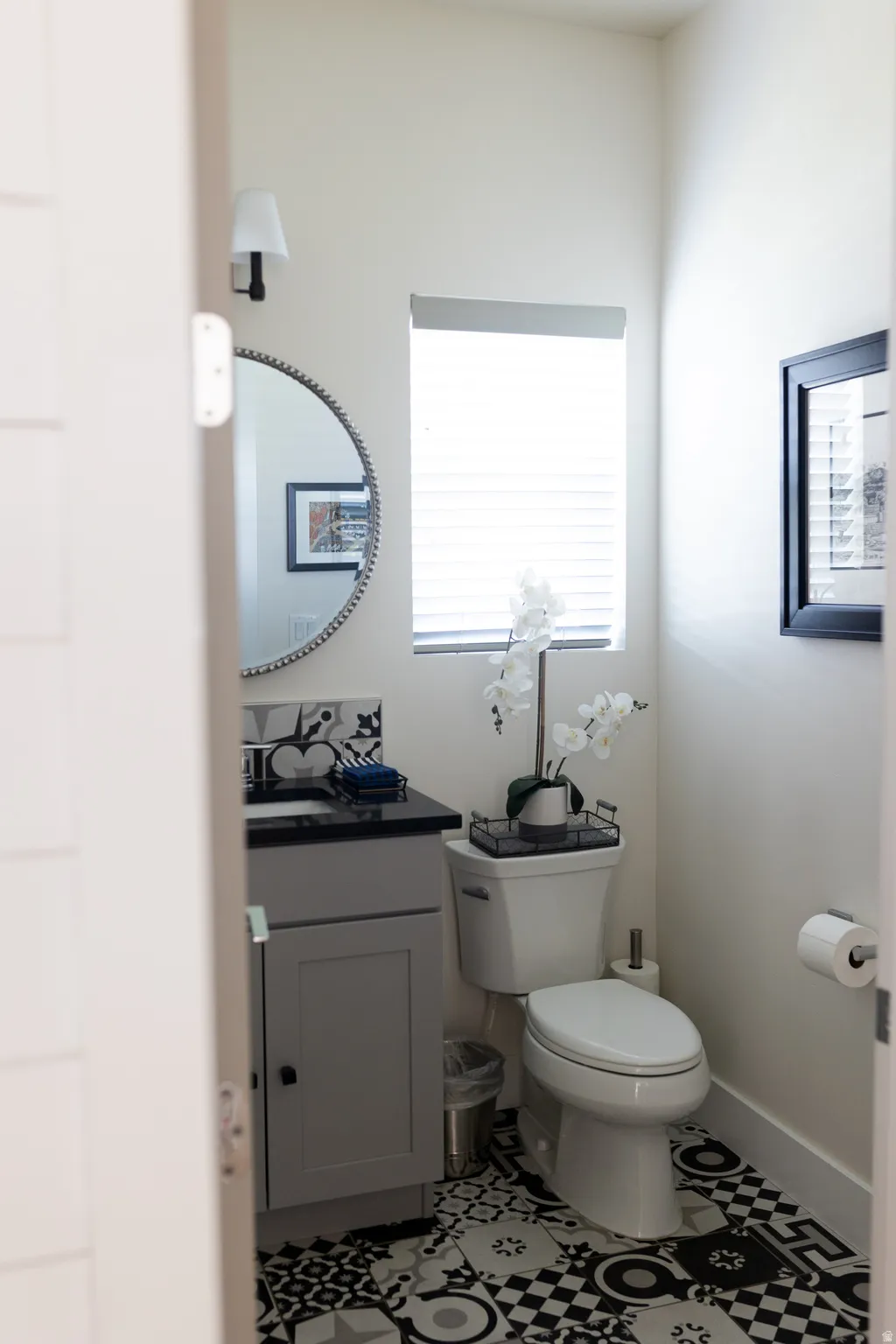 Main Floor powder room/half bath featuring a black and white patterned tile floor, a grey vanity with a dark countertop, and a round wall mirror