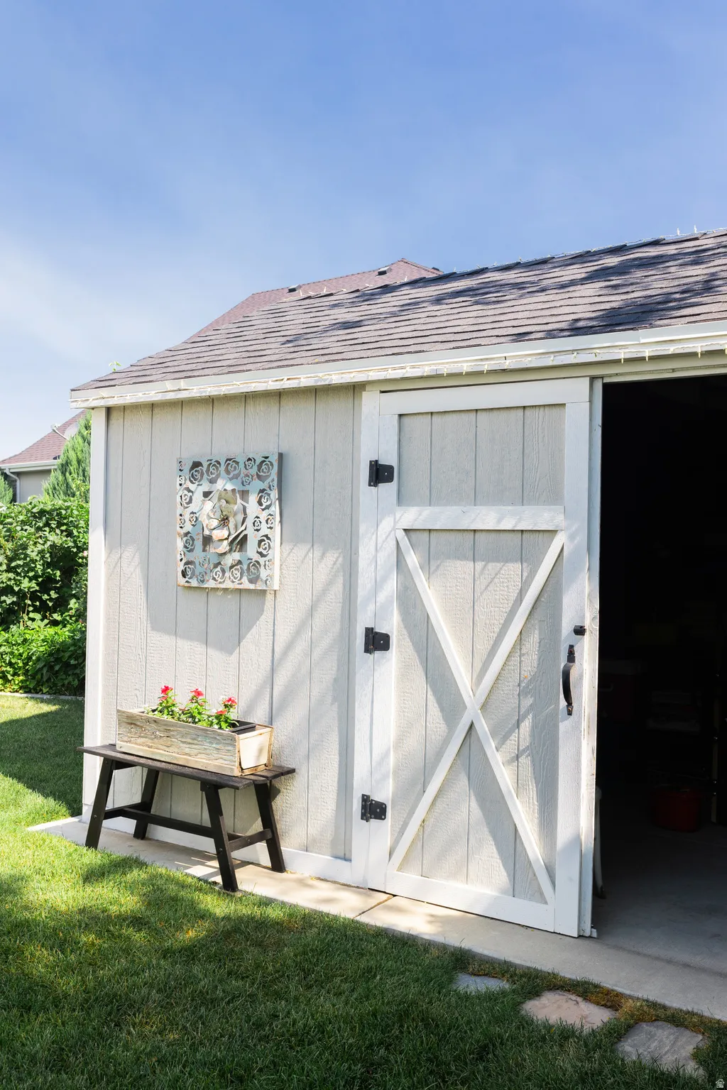 Outdoor storage shed with a shingled roof, light-colored vertical siding, and a white barn-style door with black hardware