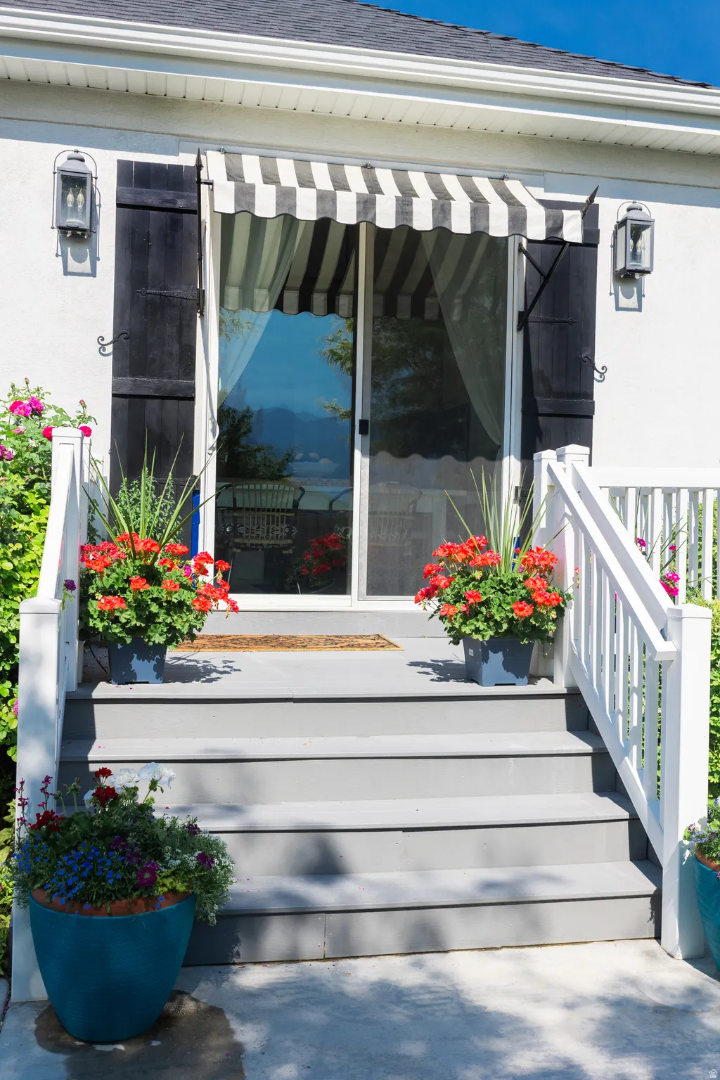 Back exterior patio entry featuring a striped awning, sliding glass door, and dark shutters