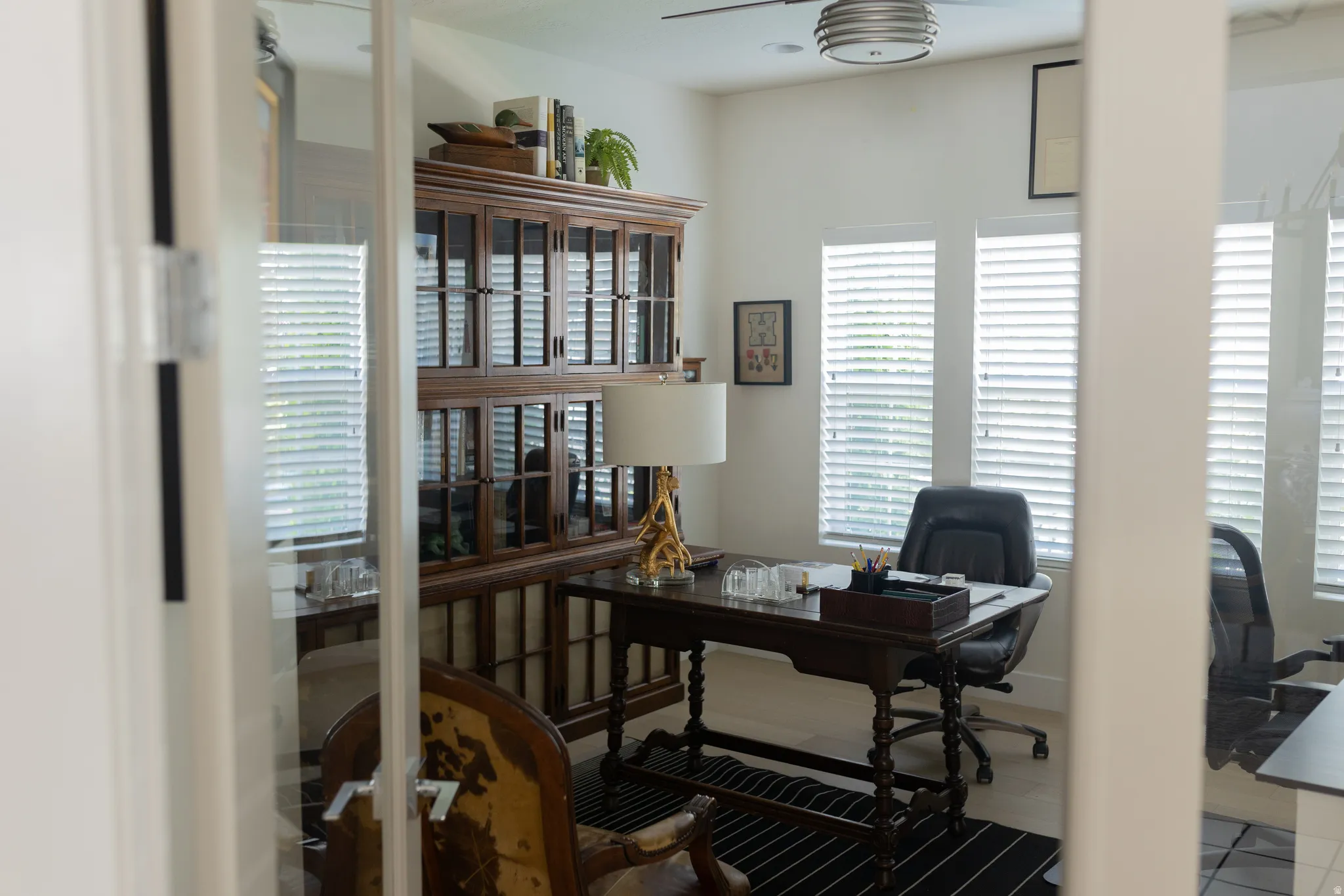 Office space featuring glass French doors, multiple windows with blinds, a ceiling fan, and light-toned flooring