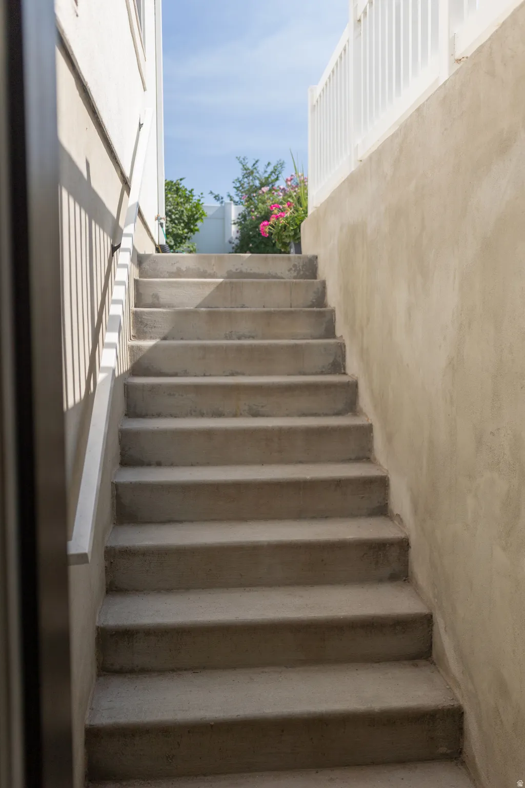 Basement mother-in-law apartment entrance on north east side of home. Concrete staircase with a metal handrail, bordered by a stucco wall and a white picket fence.