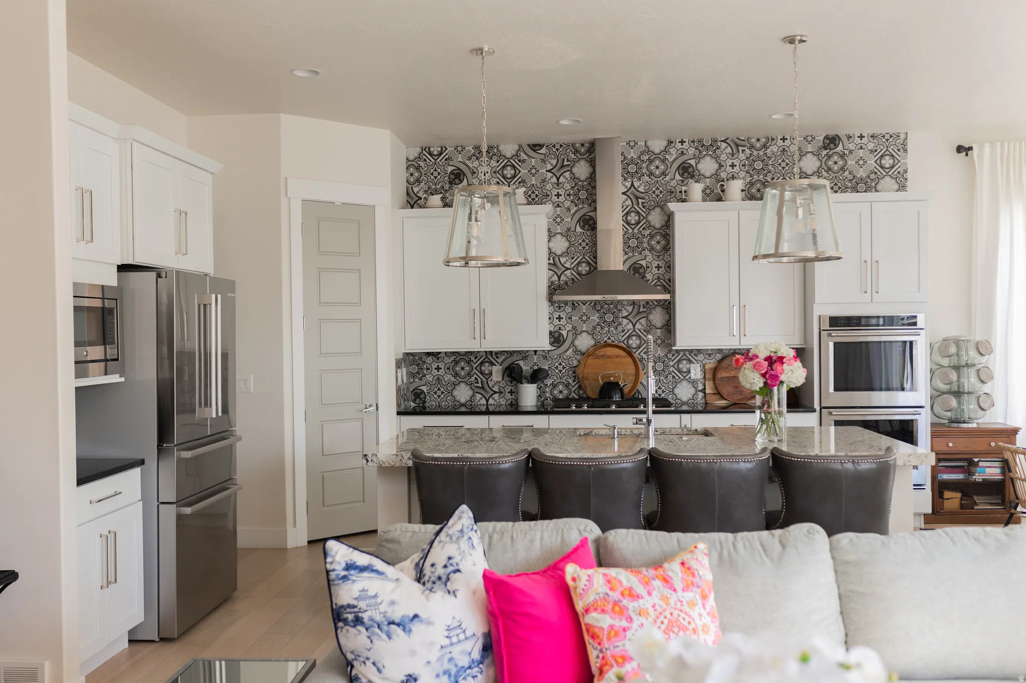 Contemporary kitchen featuring white cabinetry, stainless steel appliances, a patterned tile backsplash, an eat-at island with granite-finish countertop, and pendant lighting