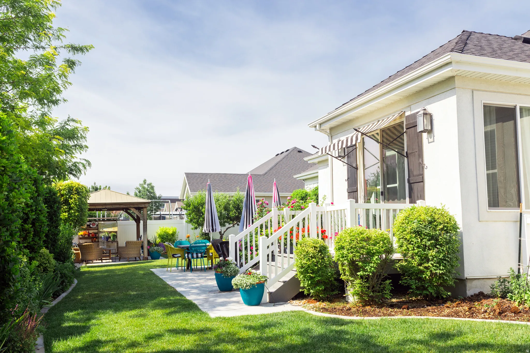 Backyard from north east corner with a white exterior home featuring a striped awning and dark wood shutters