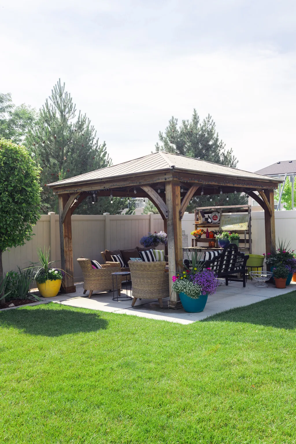 Backyard featuring a wood-frame gazebo with a metal roof, a concrete patio, a manicured lawn, and perimeter fencing.