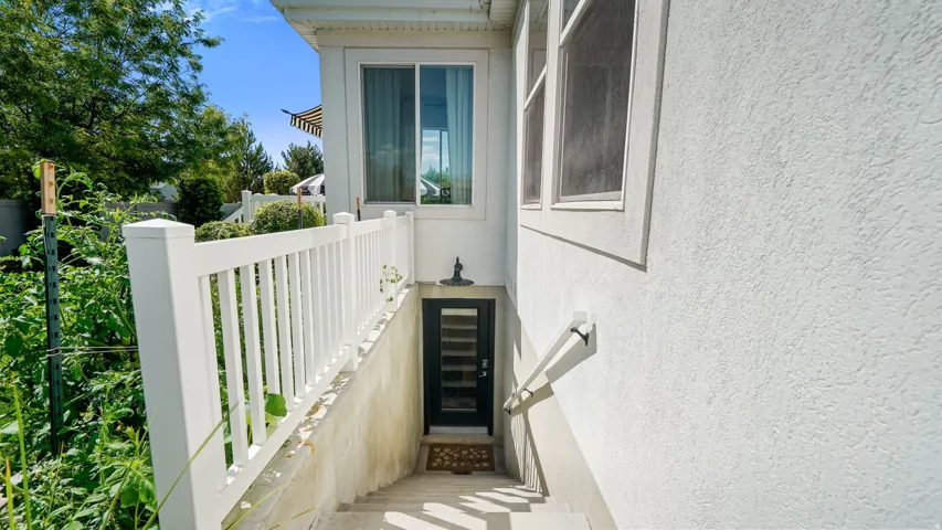 Exterior basement entrance featuring a black door, concrete steps, white railings, and a wall-mounted handrail