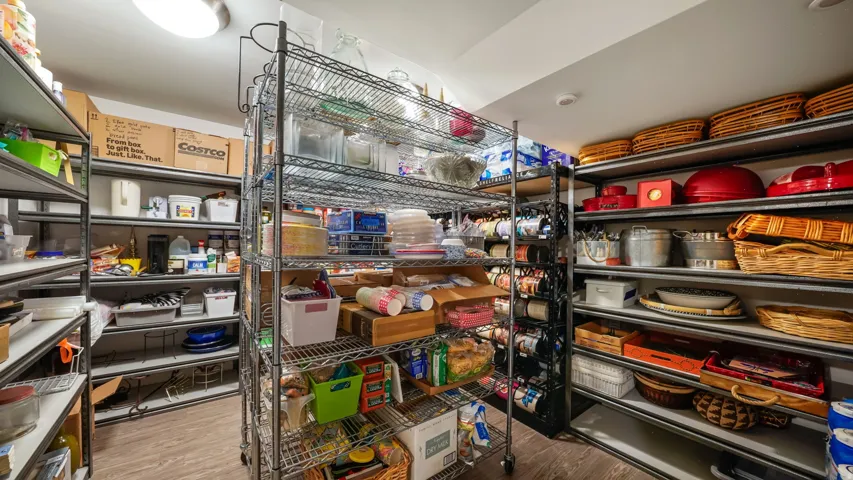Spacious pantry featuring multiple levels of shelving, integrated lighting, and wood-finish flooring
