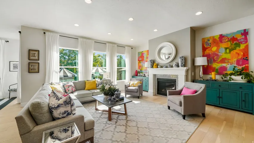 Expansive living space featuring a white mantel fireplace, light wood-finish flooring, recessed lighting, multiple large windows, and an open layout