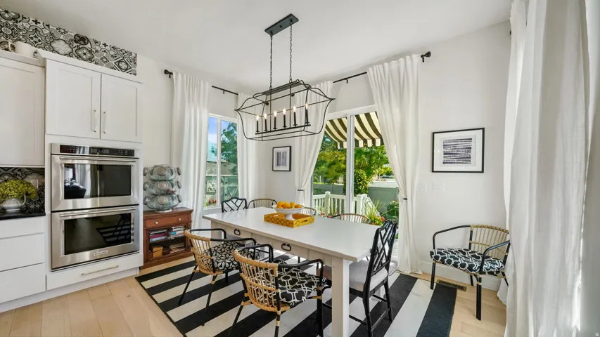 Open-concept dining area featuring light wood-finish flooring, a contemporary chandelier, and direct access to an outdoor space with a striped awning