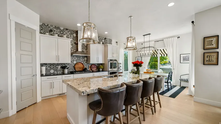 Gourmet kitchen featuring a large island with seating, white cabinetry, patterned tile backsplash, stainless steel appliances, and light wood-finish flooring