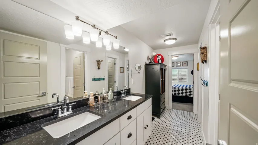 Dual vanity with black stone countertop, integrated sinks, chrome fixtures, and overhead bar lighting