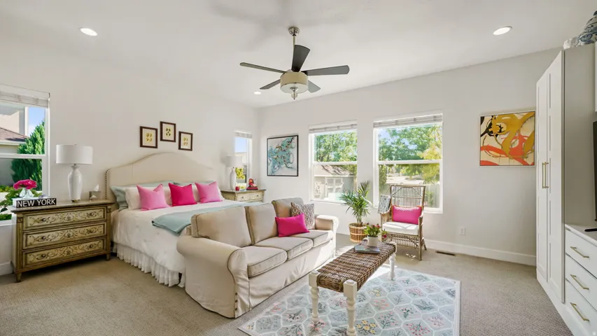 Spacious primary bedroom suite featuring multiple large windows with natural light, ceiling fan with integrated lighting, neutral wall finishes, and direct access to an ensuite bathroom