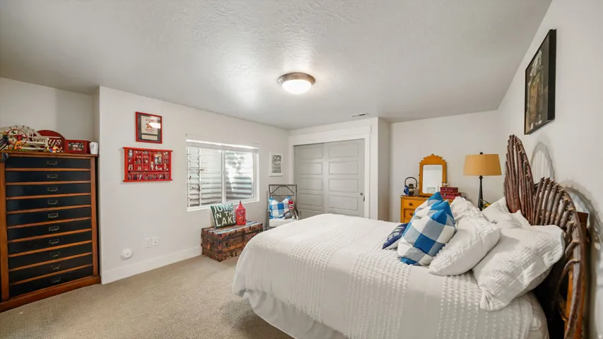 Spacious secondary bedroom featuring neutral carpeting, a wood-finish bed frame with decorative headboard, dual nightstands with lamps, and ample natural light from shuttered windows